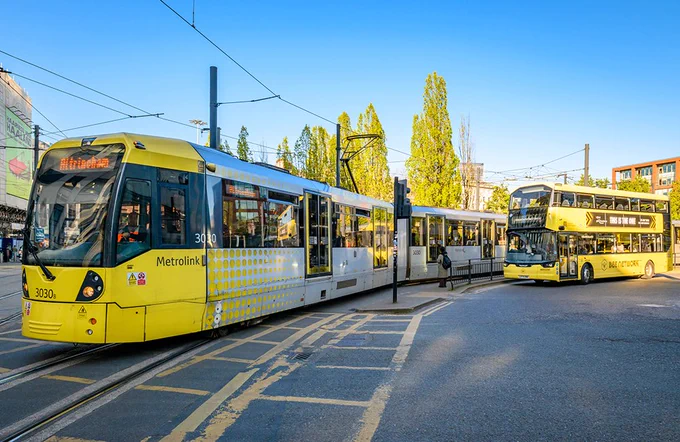 Yellow tram and double-decker bus on a city street in Manchester.