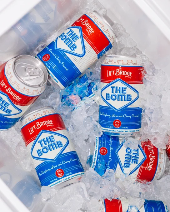 Several cans of Lift Bridge's 'The Bomb' drink are chilled in a cooler filled with ice. The colorful design and bright setting evoke a refreshing and vibrant mood.