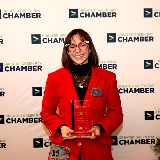 A person stands holding an award, wearing a red outfit and patterned glasses.
