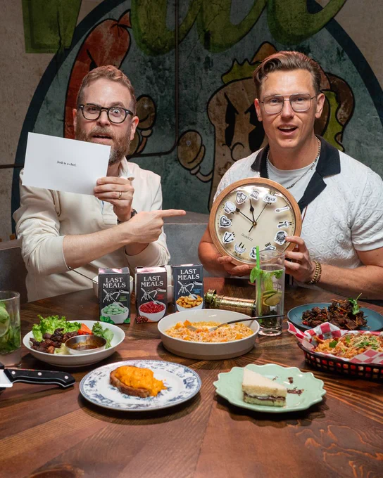 Sam and Chef Josh on the set of Last Meals, holding up elements of an "escape room in a box" made for Sam to solve.