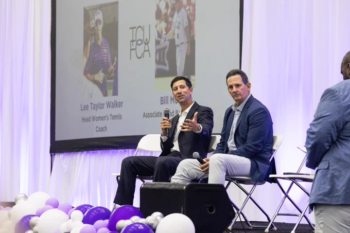 Two individuals sit on a stage holding microphones during a discussion. A large screen behind them displays images and text, including "Lee Taylor Walker" and "Bill Hill," with brief titles. The stage is decorated with white and purple balloons, and there’s an audience member in view.