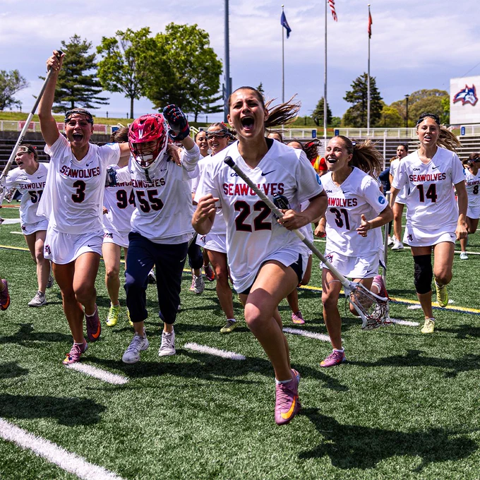 Women’s lacrosse players run across the field celebrating after a game.