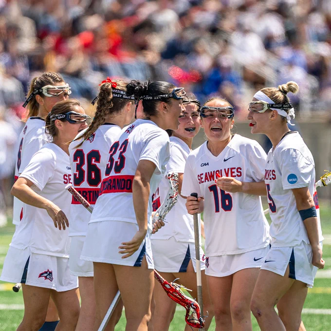 Stony Brook women’s lacrosse players celebrate together in a huddle on the field.