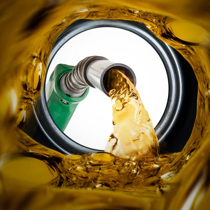 Photo of a gas station dispenser nozzle pumping fuel into a car.