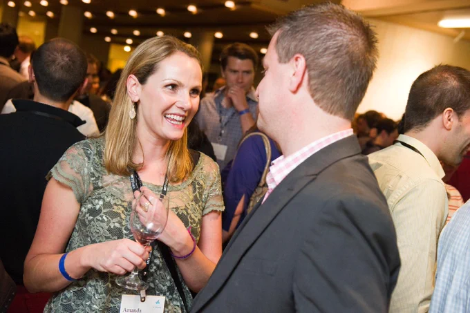 A smiling woman speaks to a man in a crowd of people at a social event.