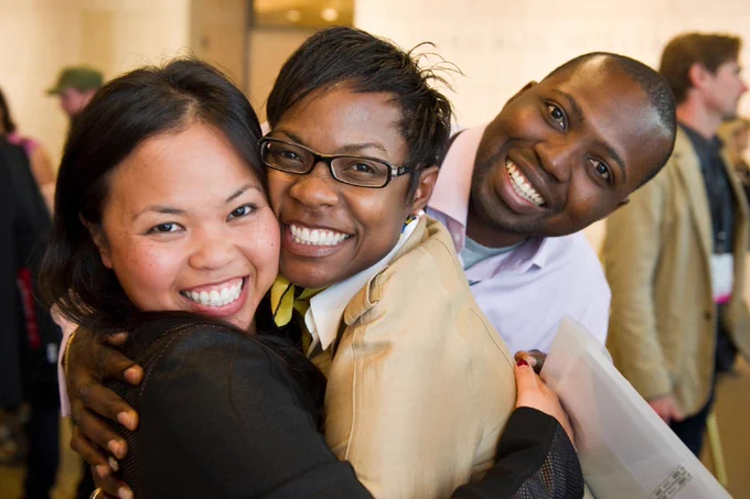Two hugging women and a man next to them smile for a photo.