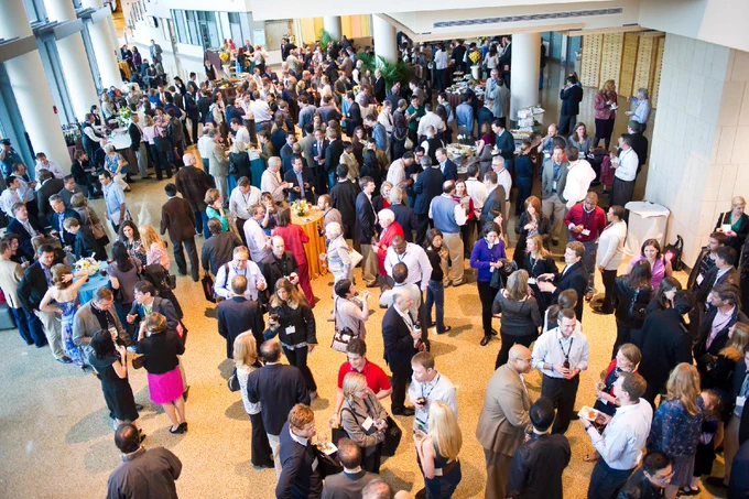 A large crowd of people gathers for a social event in a building lobby.