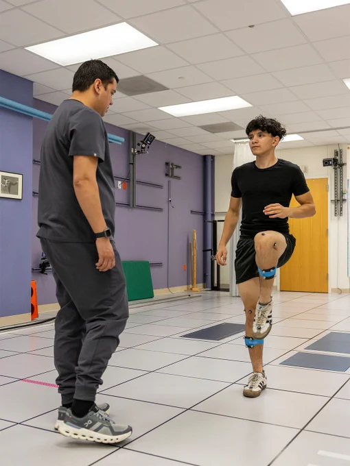 Physical therapist observing a young man performing a knee lift exercise in a motion analysis lab.