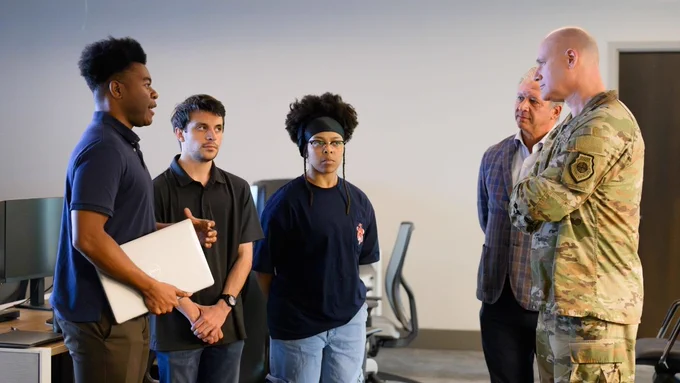 Image of five people standing in a room talking.