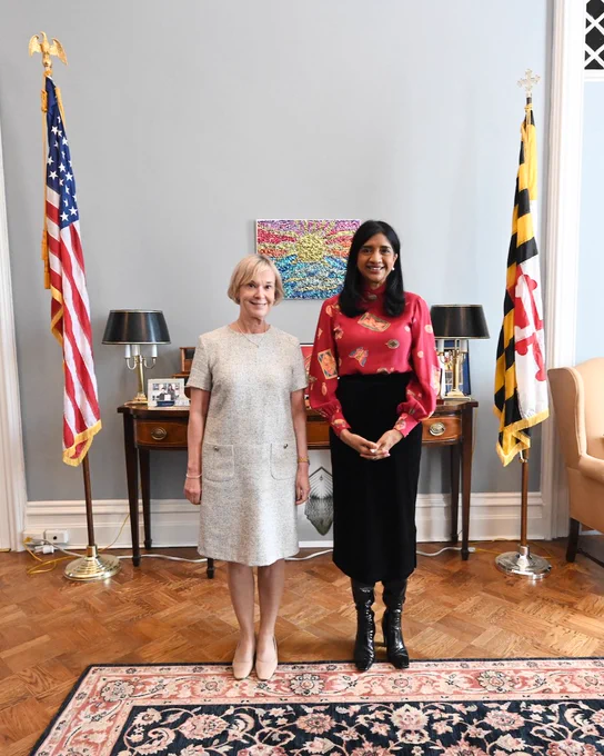 Ambassador and Lt. Gov. Miller standing in front of a grey wall and furniture.