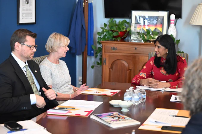 Ambassador, Miller, and staff sitting at a dark brown table for a discussion.