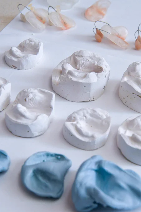 A collection of white and blue plaster dental molds arranged neatly on a flat surface, with wire loops attached to some molds for display purposes.