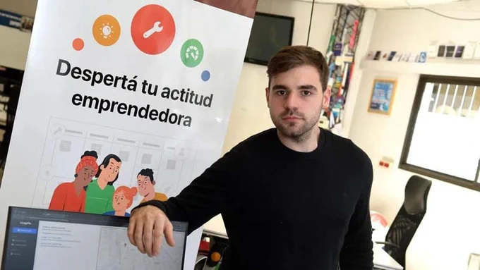 Persona joven en el Centro de Innovación y Emprendimientos de ORT junto a un cartel: "Despertá tu actitud emprendedora".