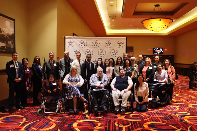 Access Board Members and staff stand in front of a banner displaying the Access Board logo.