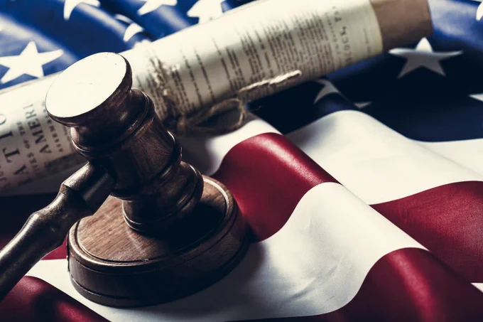 A wooden gavel lies on an American flag with a rolled parchment document in background. 