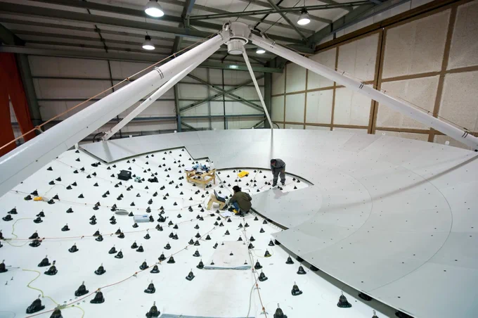 In the photo, two engineers are working on the dish of a European antenna for ALMA, installing the metal panels that make up the reflective surface. 
The dish is 12 meters in diameter!📡
