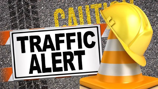Traffic alert sign with orange and white striped barricade, yellow construction cone, and hard hat on asphalt with faded caution text.