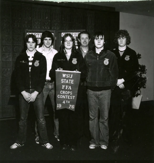 Black and white photo of 6 people wearing FFA jackets with one in the center holding a banner that says WSU State FFA Crops Contest 1976, 4th.