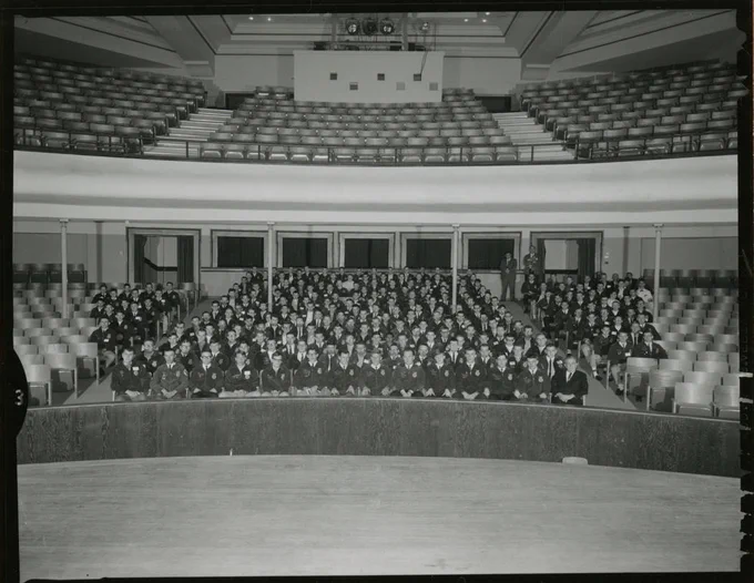 Black and white group shot of over 100 people wearing FFA jackets sitting in a large auditorium.