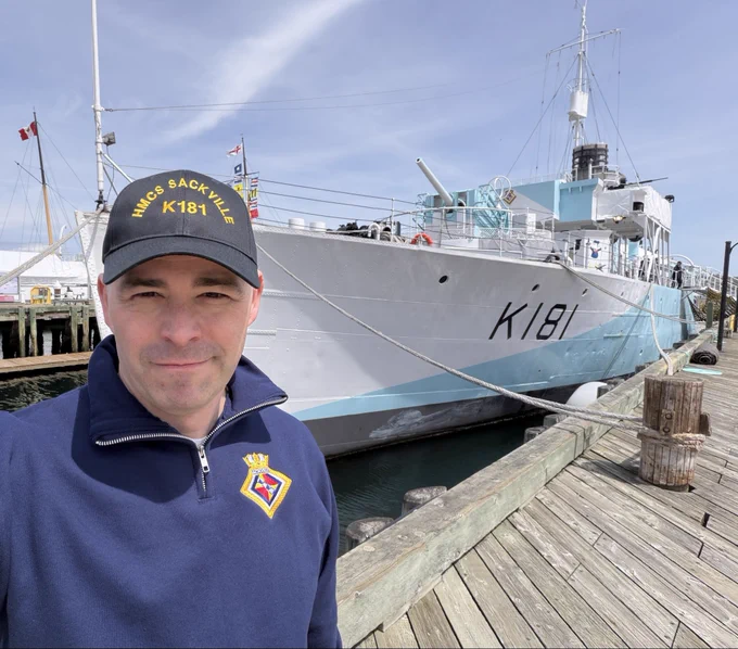 Picture of Stephen Brosha standing in front of HMCs Sackville on the Halifax waterfront on a blue-sky day.