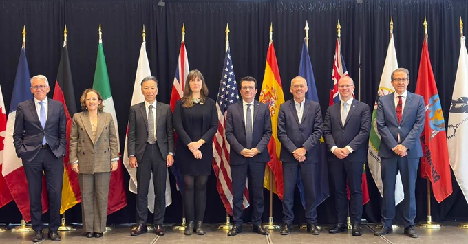 IMAGE: Representatives of various countries attending the R7  conference in Ottawa in November 2025. They are posing for an official portrait on the stage in front of a series of international flags.