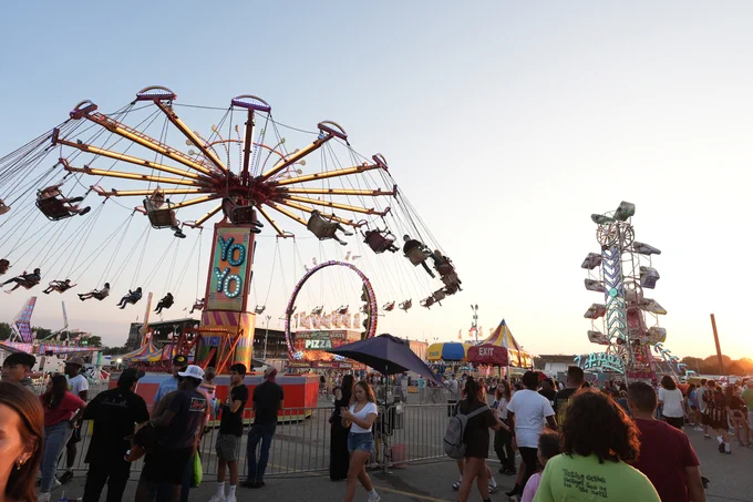 A photo of Thrill Ville at the Iowa State Fair. A giant swing ride is in the center of the photo with multiple Fairgoers walking around the area at the bottom of the photo.