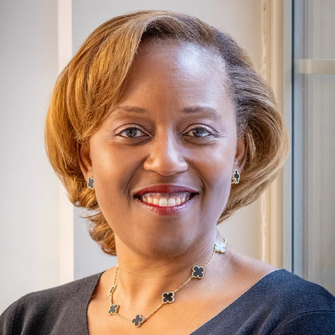 Professional headshot of Christine Miller, smiling and wearing a dark navy top and a gold and green four-leaf clover necklace and earrings.