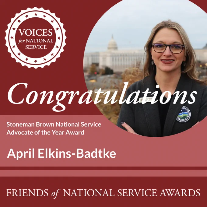 Congratulations message for the Stoneman Brown National Service Advocate of the Year Award. The image features a person standing outside with the U.S. Capitol in the background. The text includes "April Elkins-Badtke" and "Voices for National Service."