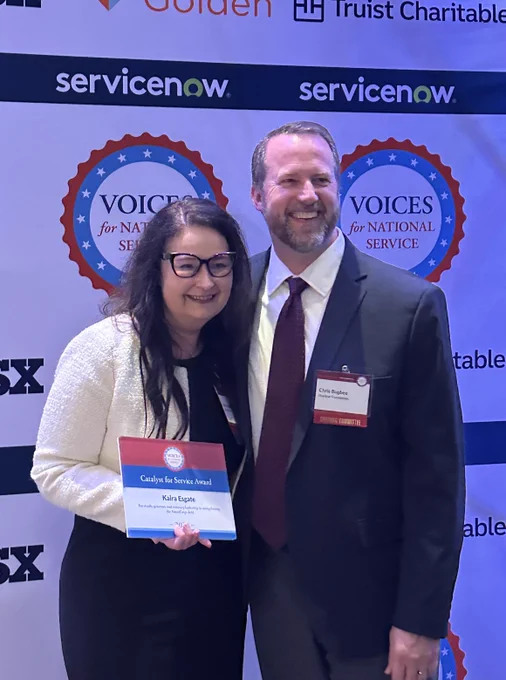 Two people smiling with plaque "Catalyst for Service" award.