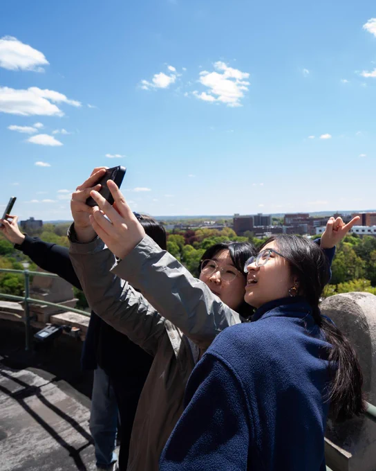 Three students taking a selfie on the balcony of Rush Rhees Library. 
