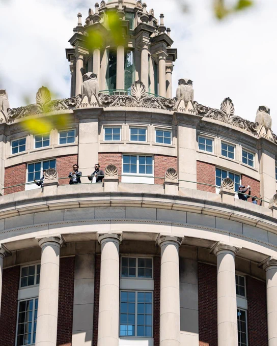 A group of students waving from high atop Rush Rhees Library tower. 
