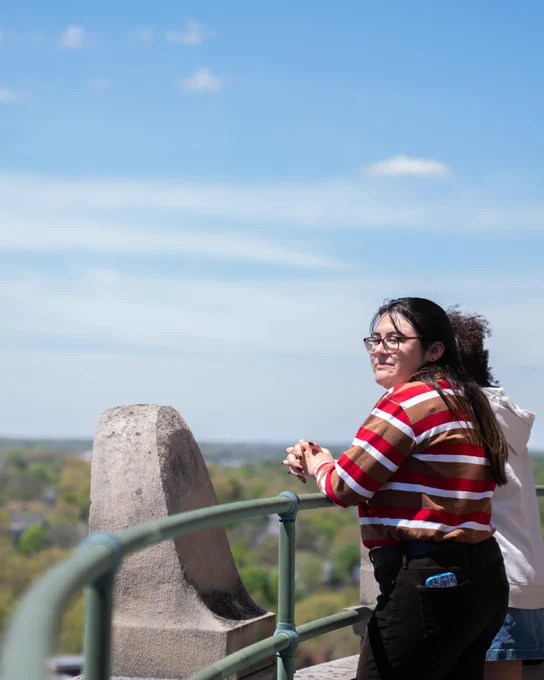 A student looks over the railing and into the distance from the Rush Rhees Library tower. 
