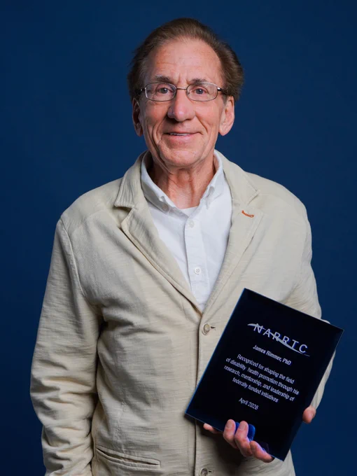 Dr. James Rimmer smiling for a photo while holding the Distinguished Service Award from the NARRTC.
