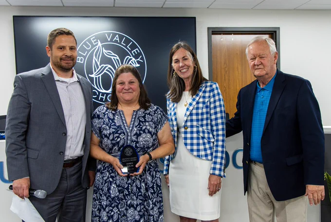 Blue Valley Schools' Karen Tolar holding an Distinguished Service Award, standing and smiling with district leadership.