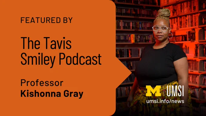"Featured by The Tavis Smiley Podcast. Professor Kishonna Gray." Gray stands in front of shelves filled with books, which are bathed in red lighting. "umsi.info/news."