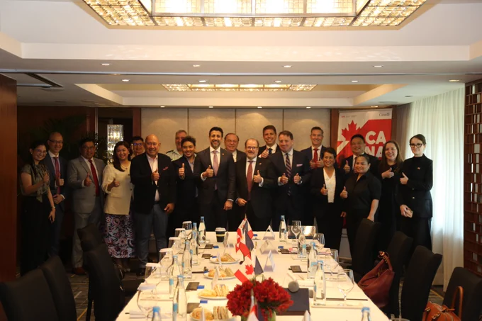 Minister Sidhu standing with a group of people in a boardroom. In front of them is a table.
