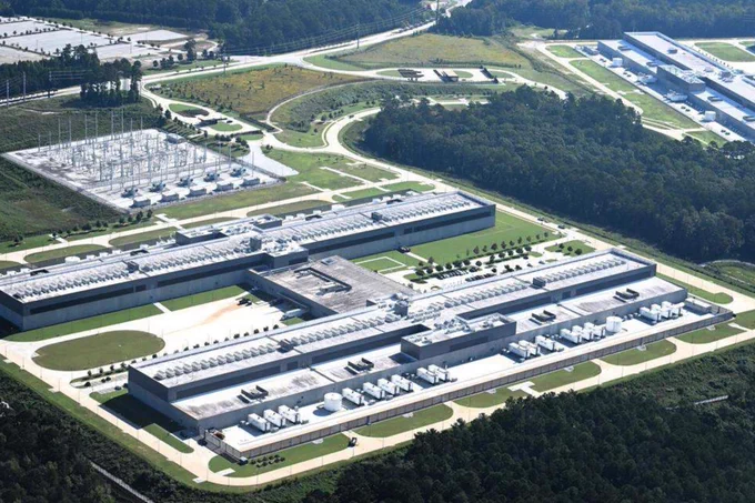 High-angle aerial view of a massive data center complex with sprawling grey buildings and heavy-duty electrical infrastructure carved into a cleared forest landscape.