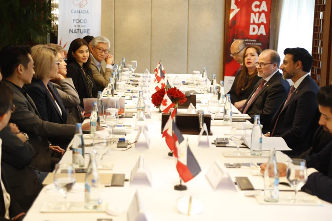 Le ministre Sidhu est assis à une table face à un groupe de personnes. Des personnes sont assises de chaque côté de lui. De petits drapeaux canadiens et philippins sont disposés au centre de la table.