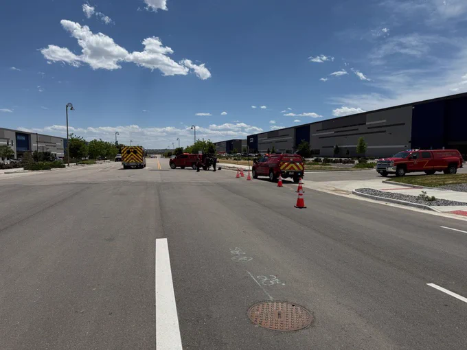 Four fire apparatus parked between two warehouse buildings with cones blocking entry.