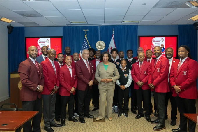 Mayor Bowser standing with members of Kappa Alpha Psi Fraternity with a blue background.