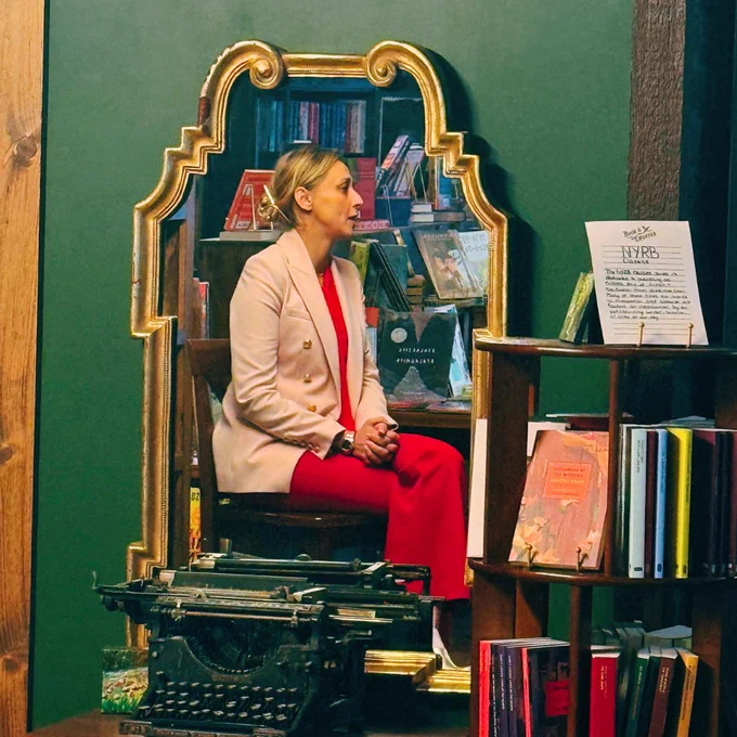 Photo of Dr. Anna Andrzejczyk speaking to attendees at the group discussion about Anti-Hormone Therapy. She is sitting on a stool in front of shelves full of books. The photo is a reflection from a mirror.