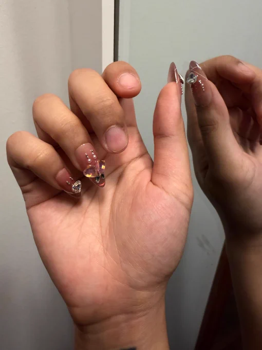 Hand with pretty bedazzled pink gradient press on nails on all fingers but the middle and index finger.