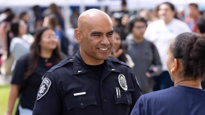 Police officer in a black uniform smiles happily as he talks to a student.