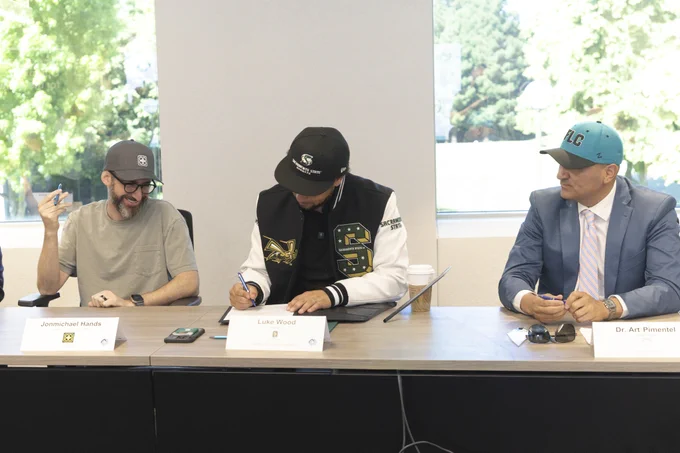 Jonmichael Hands, Luke Wood, and Dr. Art Pimentel are seated at a conference room table. President Wood is signing a document.