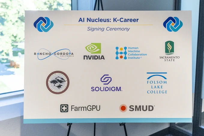 A display board titled "AI Nucleus: K-Career Signing Ceremony" with logos of Rancho Cordova, NVIDIA, Human Machine Collaboration Institute, Sacramento State, Folsom Lake College, Solidigm, FarmGPU, and SMUD.