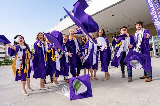 A group of graduates throws their graduation caps in front of them while they stand outside the Atlantic Union Bank Center.