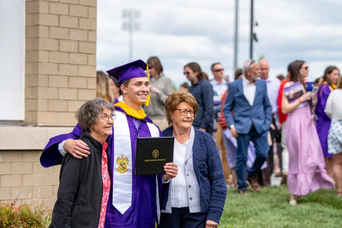 A graduate holds up their diploma case while posing for a photo.
