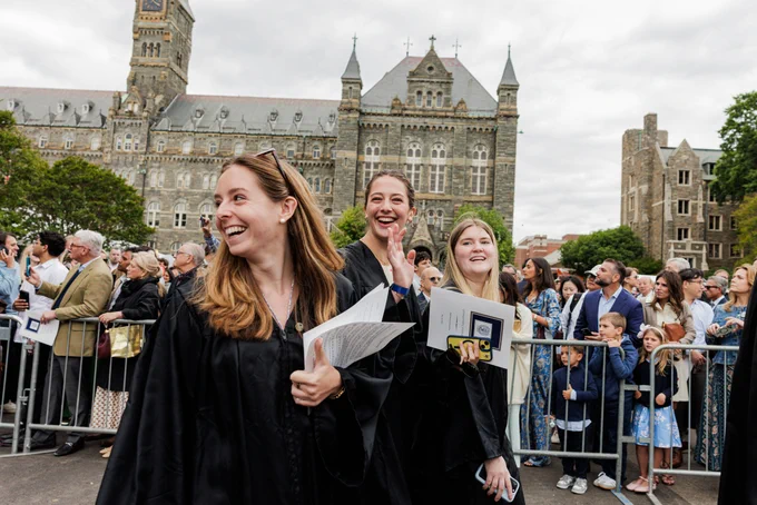 three women in robes walk past a crowd