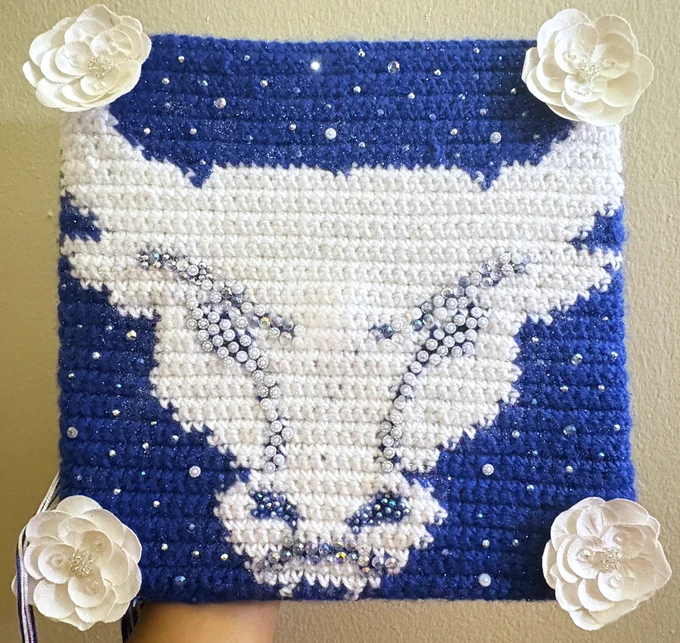 A graduation cap with a knit U B spirit mark, rhinestones, and flowers.