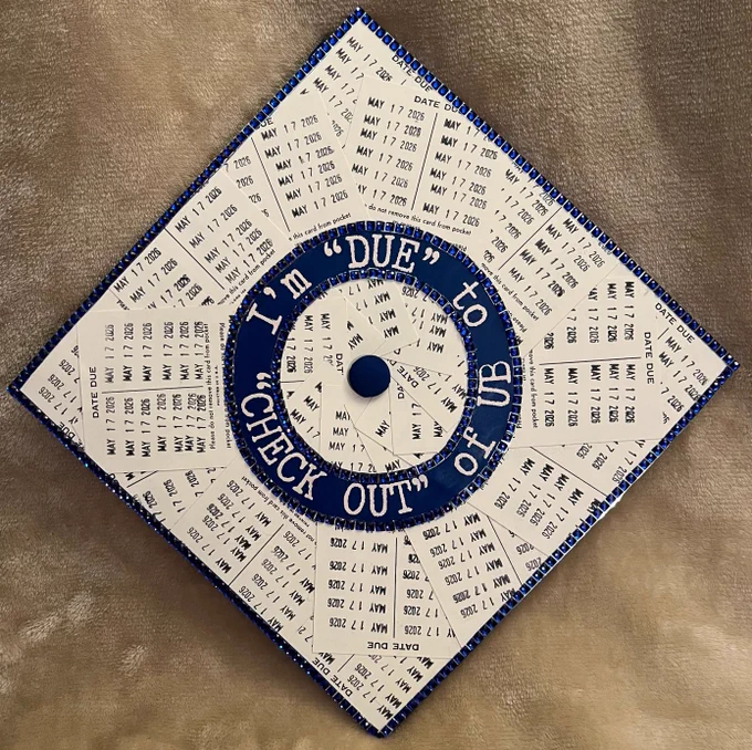 A graduation cap decorated with library check-out cards and the words \"I'm 'due' to 'check out' of U B.